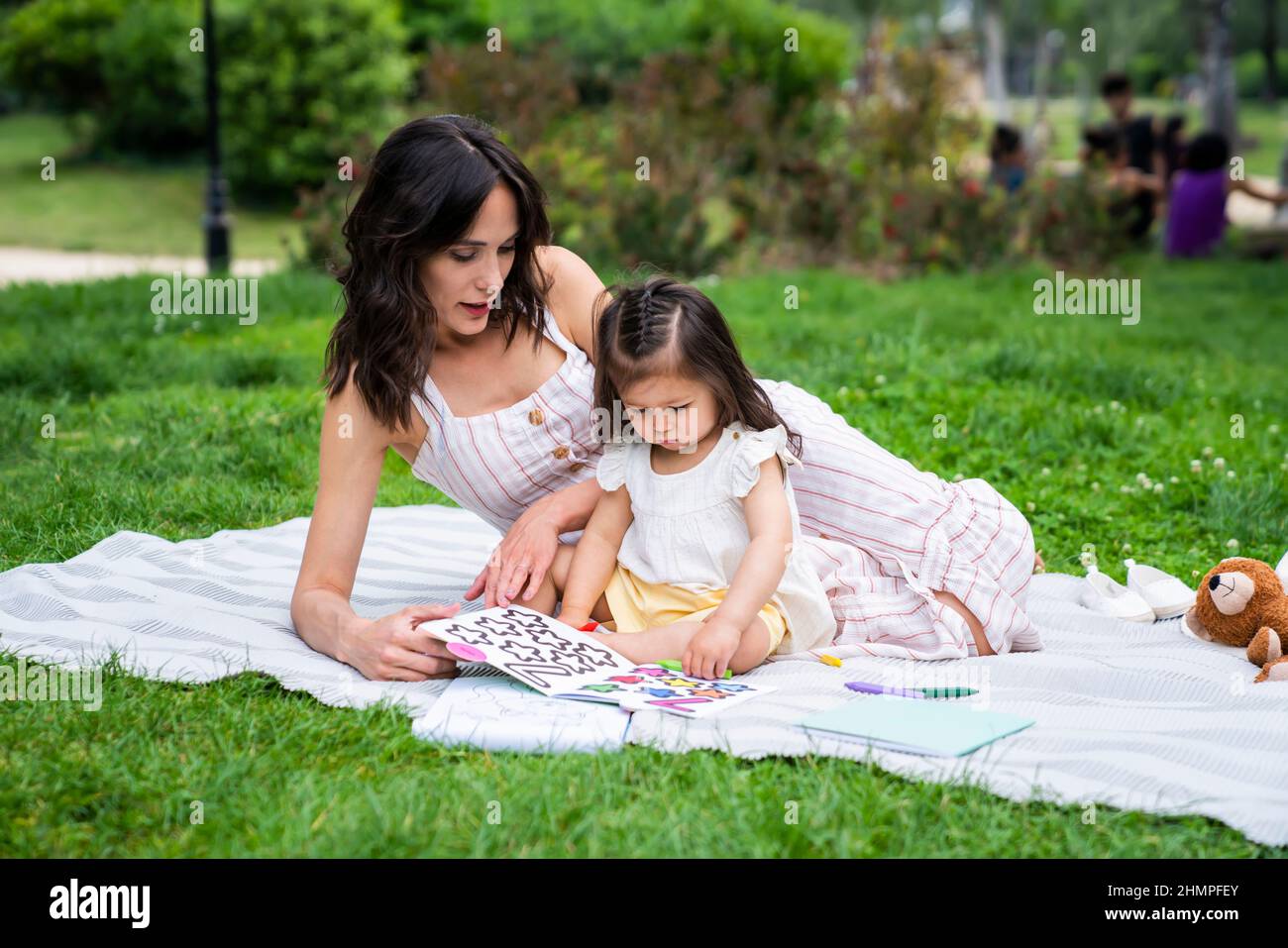 Junge attraktive Mutter sitzt auf der Decke und spielt mit Baby Mädchen im Park Stockfoto