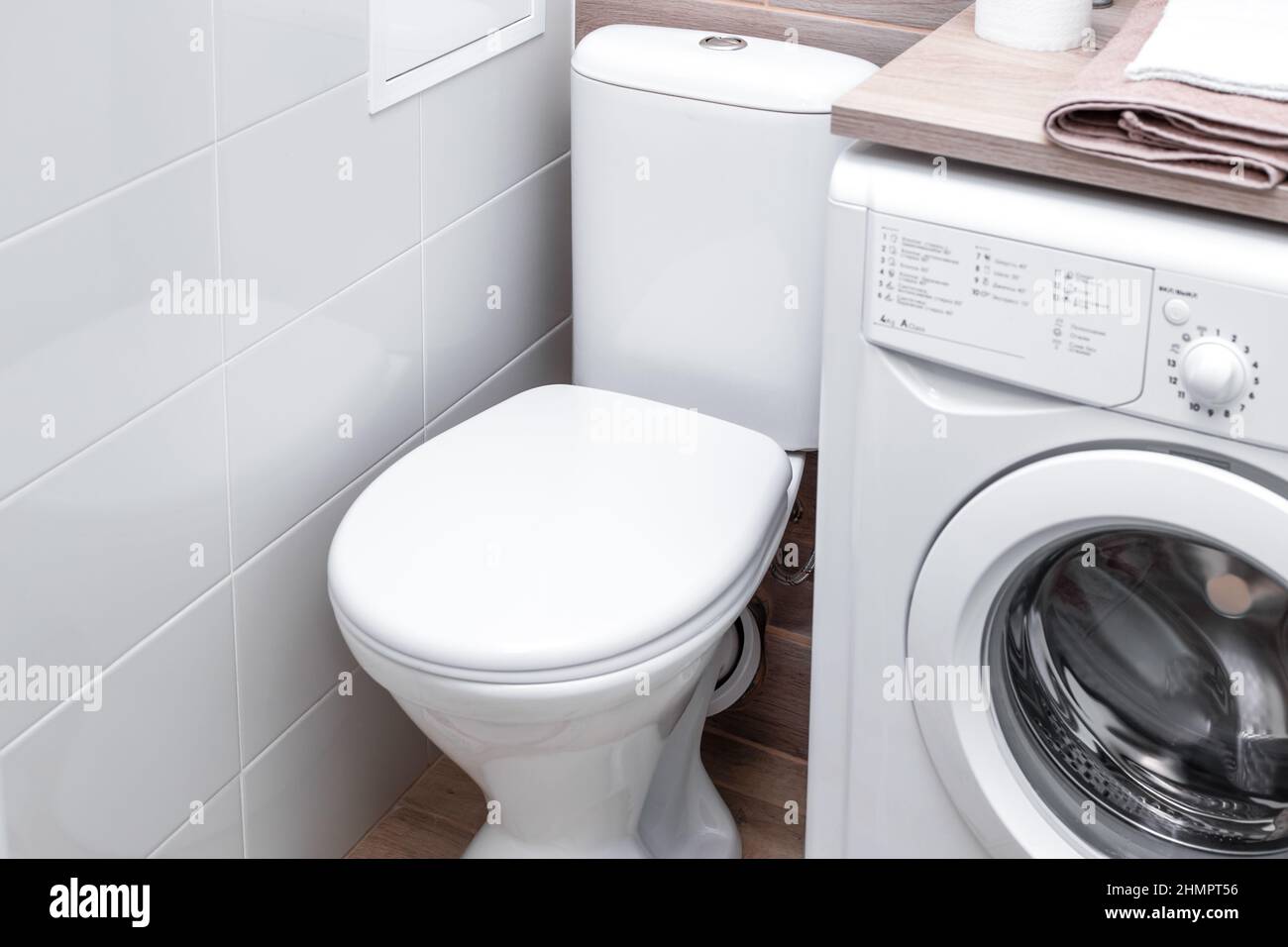 Toilettenschüssel mit geschlossenem Stuhlbezug in einem Badezimmer mit Waschmaschine. Kompaktes Layout. Stockfoto