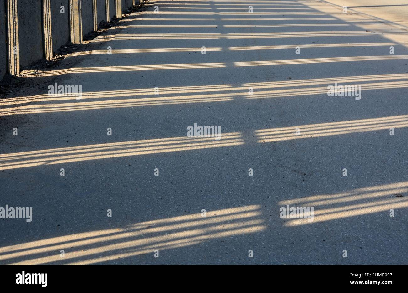 Schatten vom Zaun auf der Straße an einem sonnigen Wintertag. Ausgefallenes Muster, Spiegelung Stockfoto