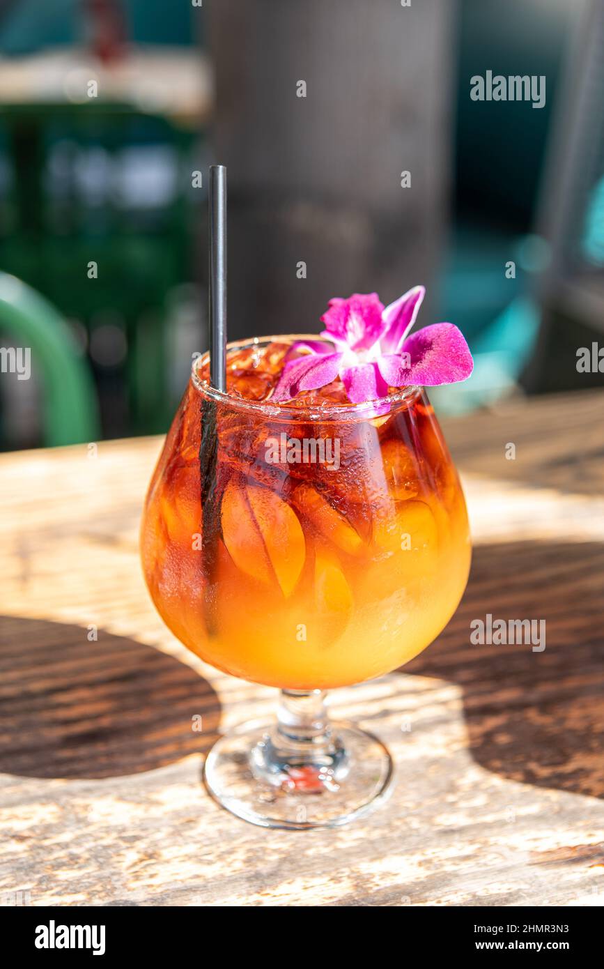 Vertikale Aufnahme eines eiskalten, köstlichen Mai Tai mit einer Blume und einem Stroh auf einem Holztisch Stockfoto