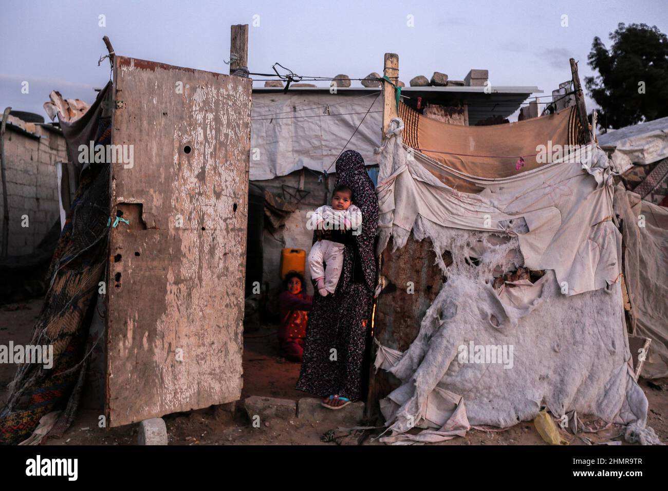 Gaza, Palästina. 10th. Februar 2022. Eine Palästinenserin hält ihr Baby, während sie bei kaltem Wetter am Rande des Flüchtlingslagers Khan Yunis im südlichen Gazastreifen vor ihrem Haus steht. Kredit: SOPA Images Limited/Alamy Live Nachrichten Stockfoto