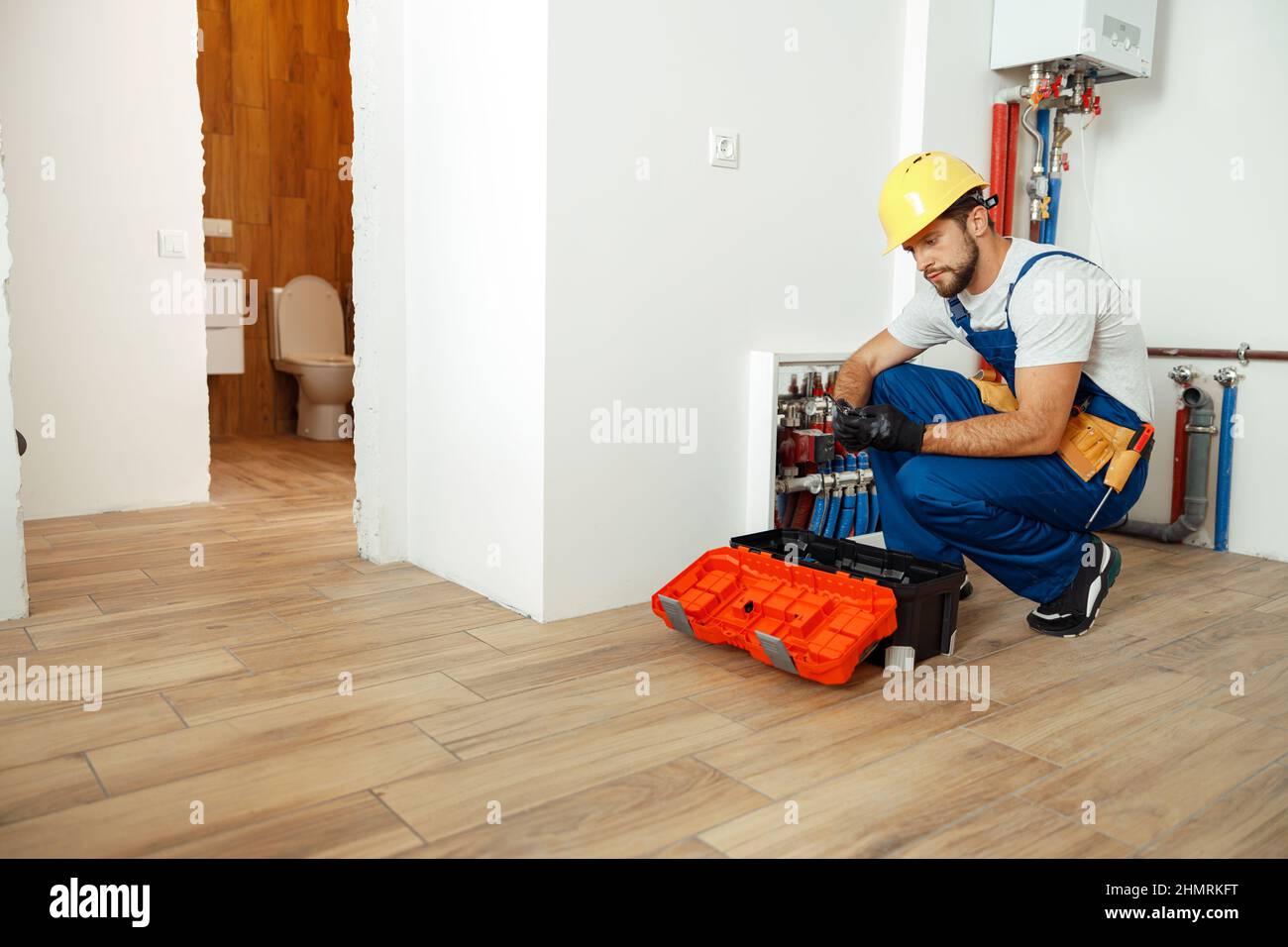 Vielbeschäftigter Techniker, Installateur in Schutzhandschuhen mit Werkzeugen aus der Werkzeugkiste beim Einrichten von Wasserleitungen Stockfoto