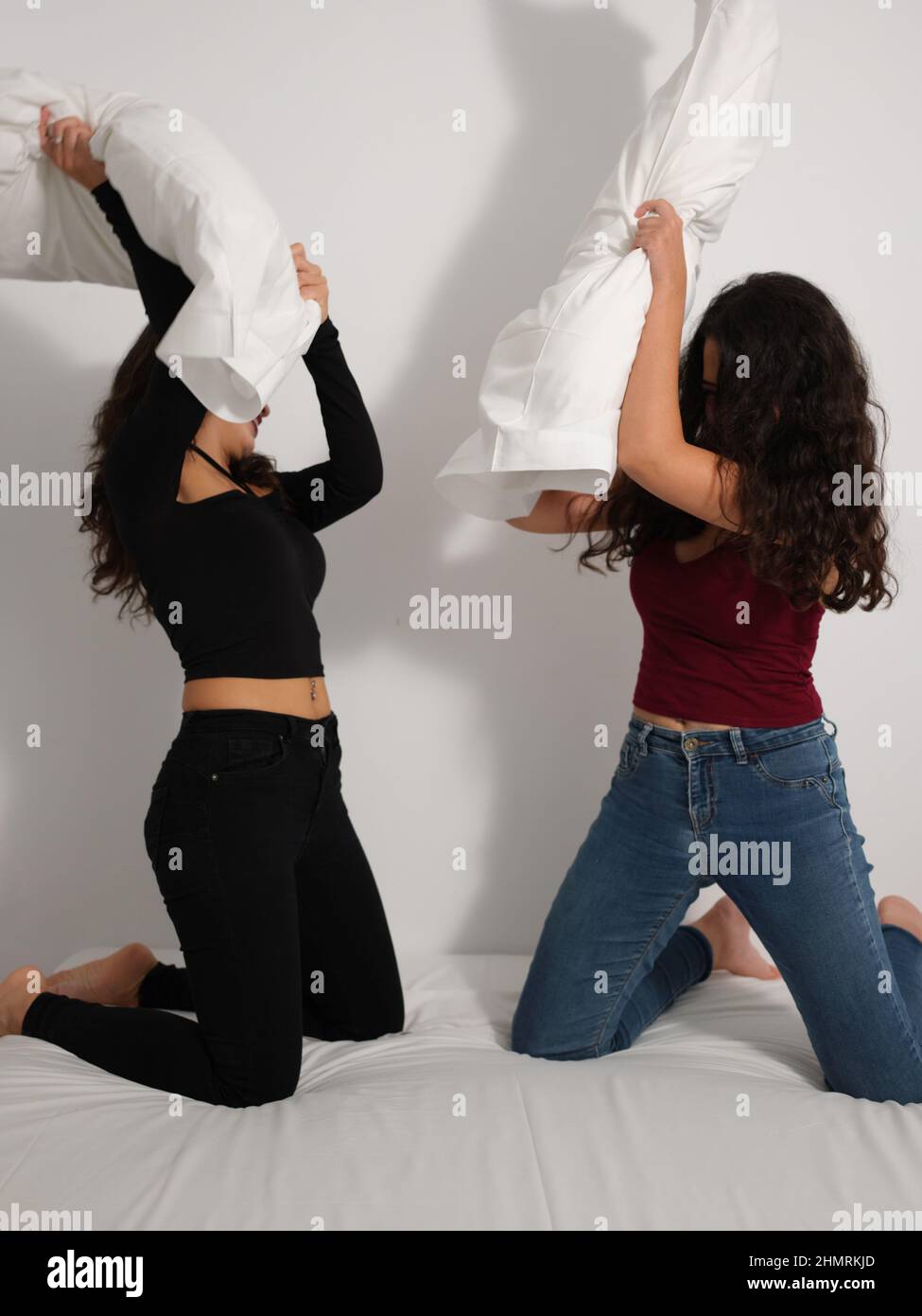 Zwei lateinische Mädchen spielen Kissenschlacht im Bett Stockfoto