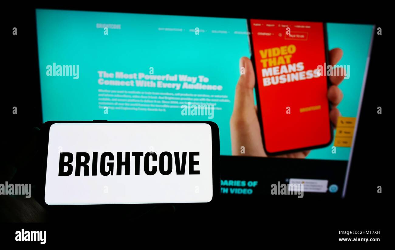 Person, die ein Mobiltelefon mit dem Logo des amerikanischen Videoplattform-Unternehmens Brightcove Inc. Auf dem Bildschirm vor der Webseite hält. Konzentrieren Sie sich auf die Telefonanzeige. Stockfoto