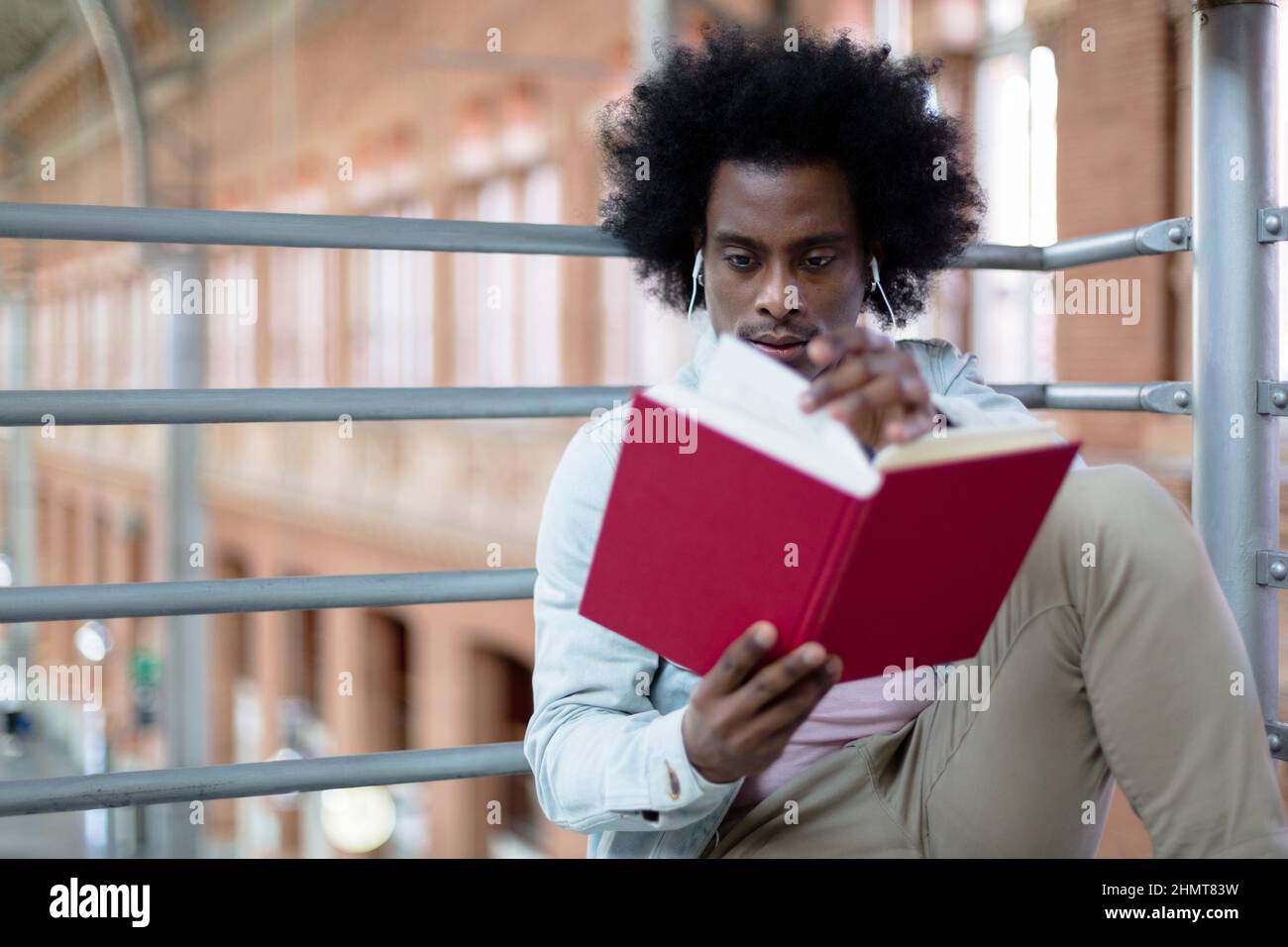 Nahaufnahme eines jungen afroamerikanischen Mannes, der an einem öffentlichen Ort ein Buch liest. Hobbys und gesunde Lebensstile. Platz für Text. Stockfoto