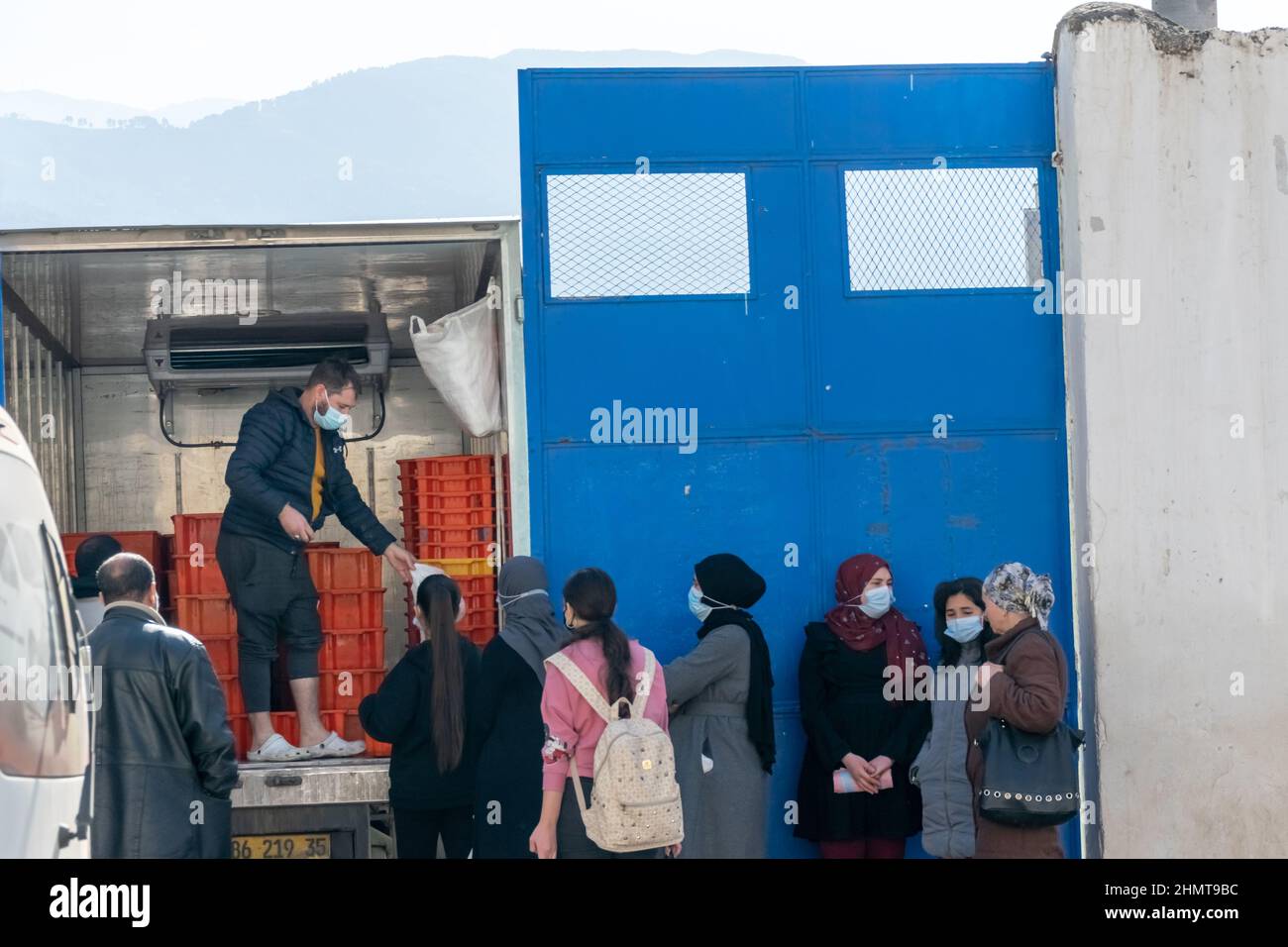 Menschen, die Lebensmittelbeutel halten, um Milchverpackungen zu kaufen auf dem Straßensteig, einem Lastwagen, der mit geöffneten Türen geparkt ist, verkauft ein Mann viele Milchkisten darin. Stockfoto