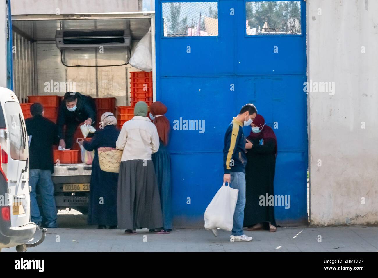 Menschen, die Lebensmittelbeutel halten, um Milchverpackungen zu kaufen auf dem Straßensteig, einem Lastwagen, der mit geöffneten Türen geparkt ist, verkauft ein Mann viele Milchkisten darin. Stockfoto