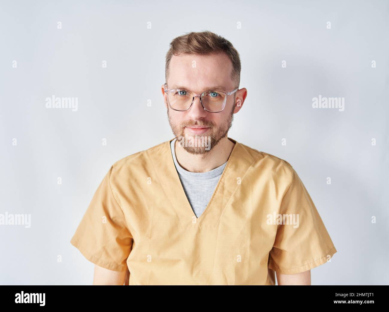 Porträt eines niedlichen jungen kaukasischen männlichen Arztes mit Brillen und beigefarbener medizinischer Uniform, der die Kamera anschaut. Nahaufnahme eines männlichen Arztes oder einer Krankenschwester im Krankenhaus. Hochwertige Fotos Stockfoto