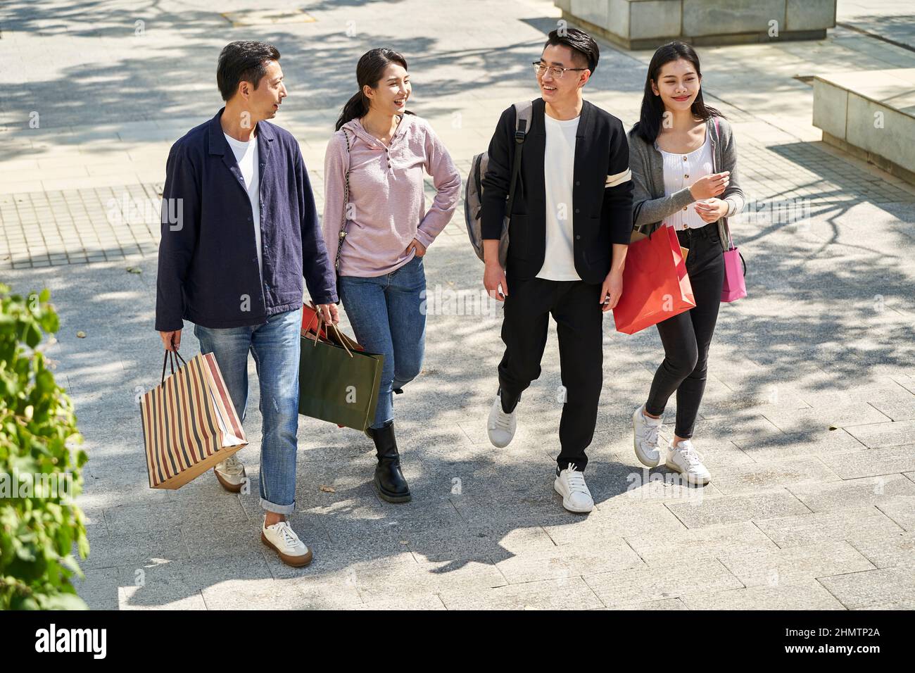Aus der Perspektive einer Gruppe von vier jungen asiatischen Menschen, die sich unterhalten und sich unterhalten, während sie mit Einkaufstaschen in den Händen auf der Straße spazieren Stockfoto