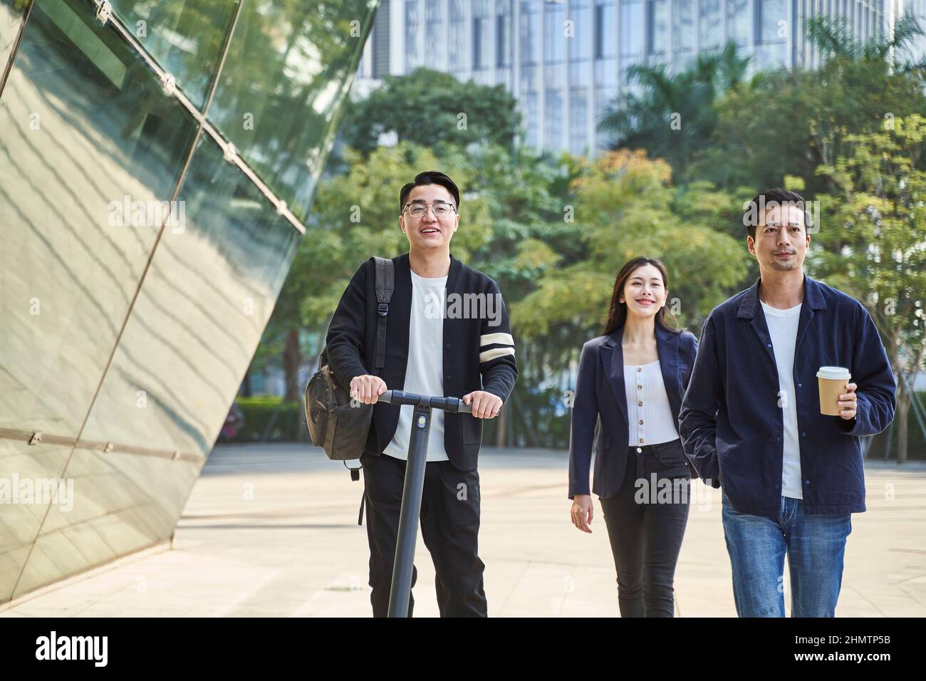 Drei junge asiatische Erwachsene, zwei Männer und eine Frau, die glücklich und lächelnd auf der Straße unterwegs sind Stockfoto