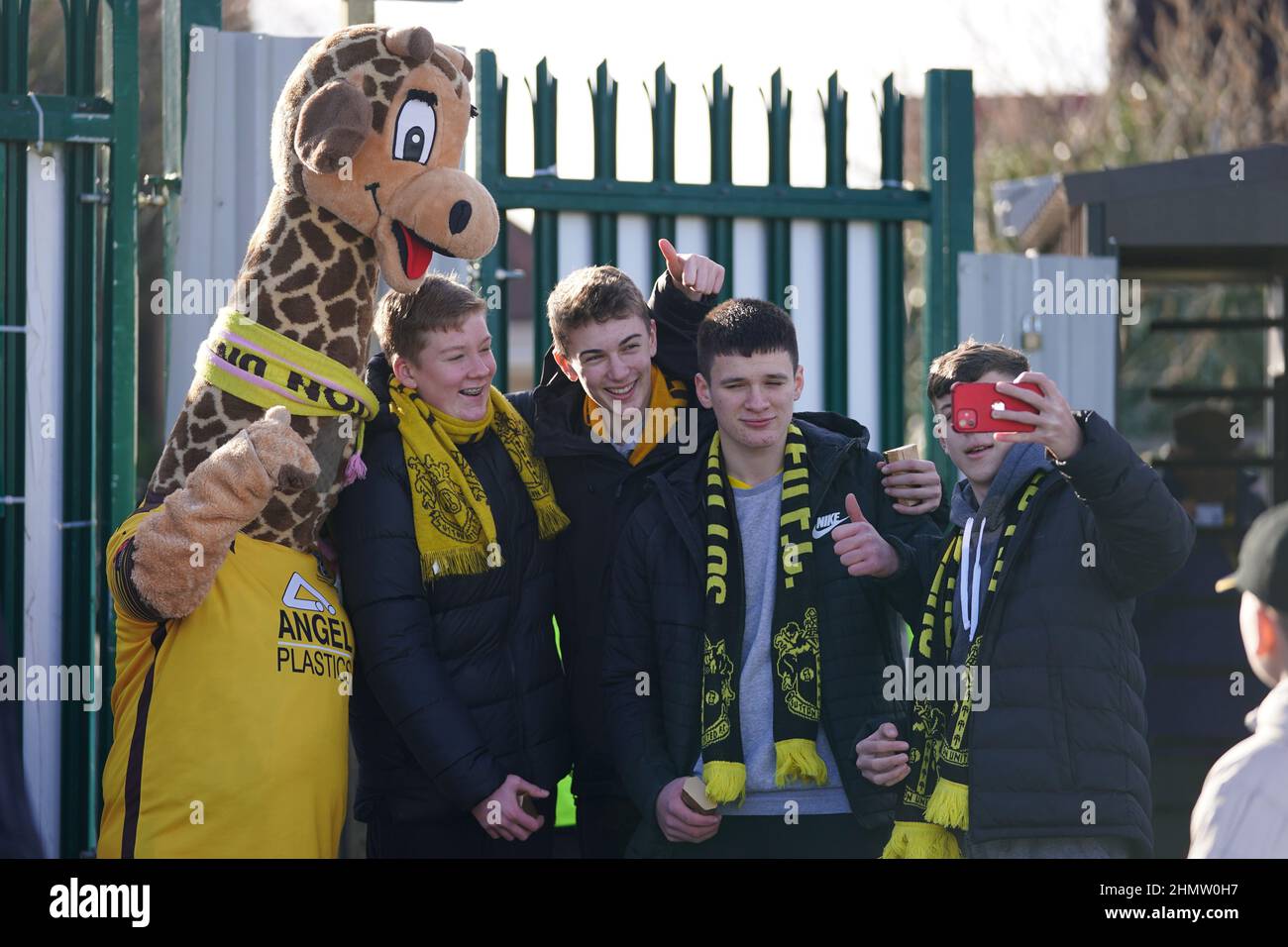 Fans von Sutton United posieren für ein Bild mit dem Maskottchen Jimmy the Giraffe vor dem zweiten Spiel der Sky Bet League im VBS Community Stadium, London. Bilddatum: Samstag, 12. Februar 2022. Stockfoto