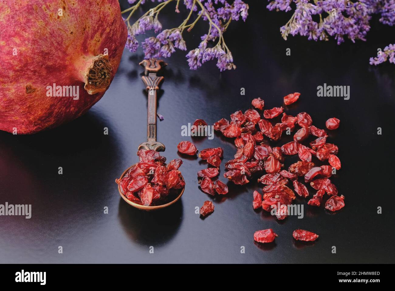 Reifer Granatapfel und organisch trockener anardana oder sonnengetrocknete Samen von Granatapfelfrüchten auf dunklem Hintergrund im Vintage cooper orientalischen Design Löffel. Stockfoto