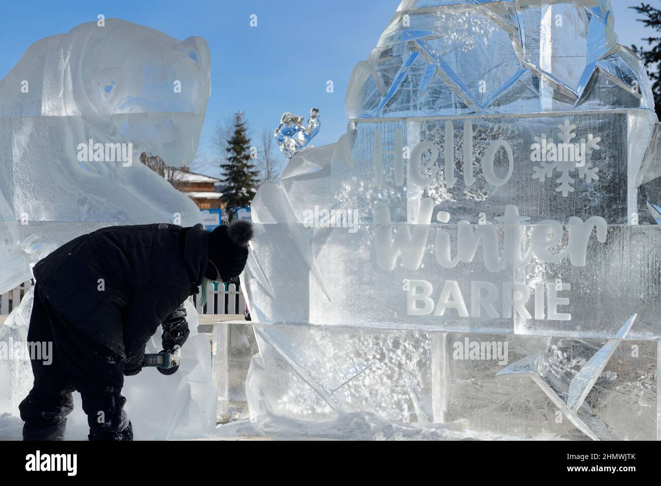 Bildhauerin, die beim Winterfest 2022 mit dem Namen Hello Winter am Meridian Place in Barrie eine Eisskulptur mit einer Eisbärschleifmaschine schnitzt Stockfoto