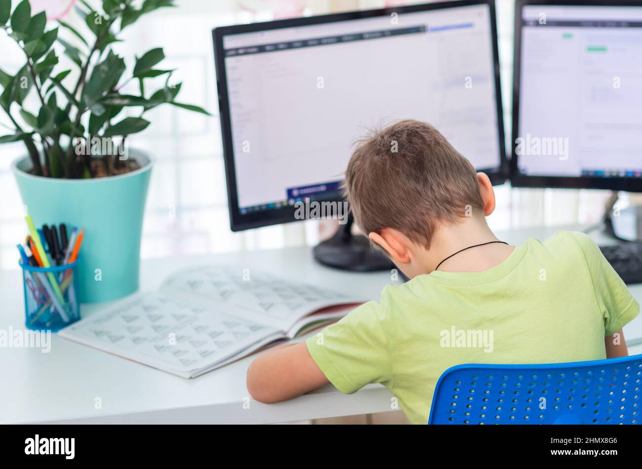 Kleiner junger Schuljunge, der zu Hause mit einem Laptop und Klassennotizen arbeitet und in einer virtuellen Klasse studiert. Fernunterricht und Lernen, E-Learning, online Stockfoto