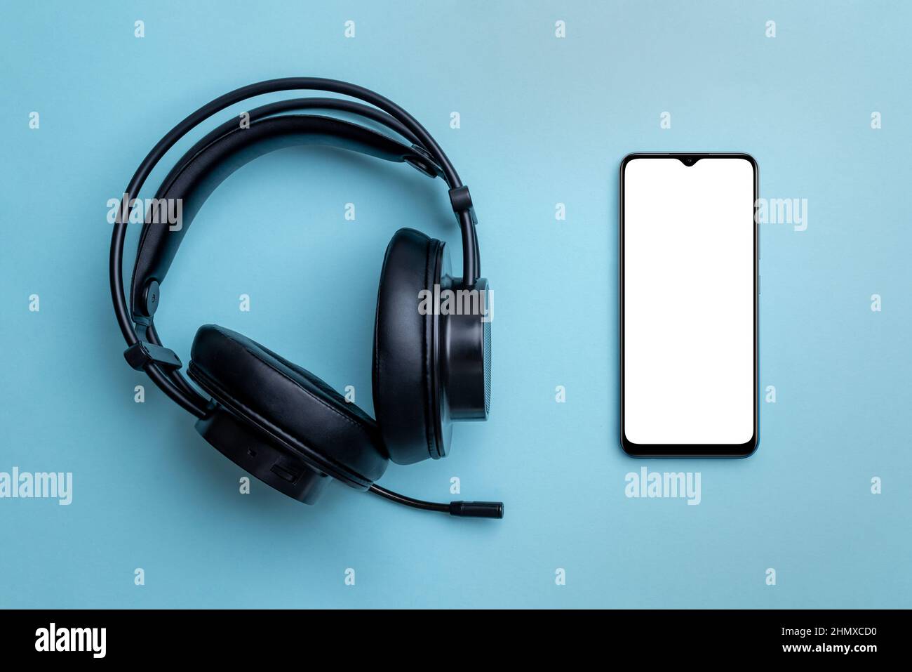 Smartphone-Mockup und kabellose Kopfhörer auf dem sauberen blauen Schreibtisch. Telefon mit isoliertem leerem Bildschirm für die App-Präsentation. Draufsicht, flach liegend Nahaufnahme Komp Stockfoto