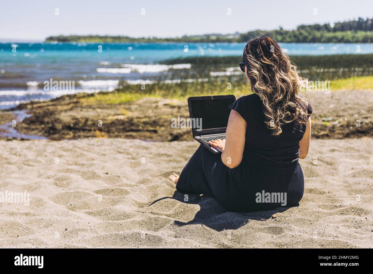 Junge Frau, die vom Strand aus Remote-Online-Arbeiten macht. Telearbeitskonzept. Stockfoto