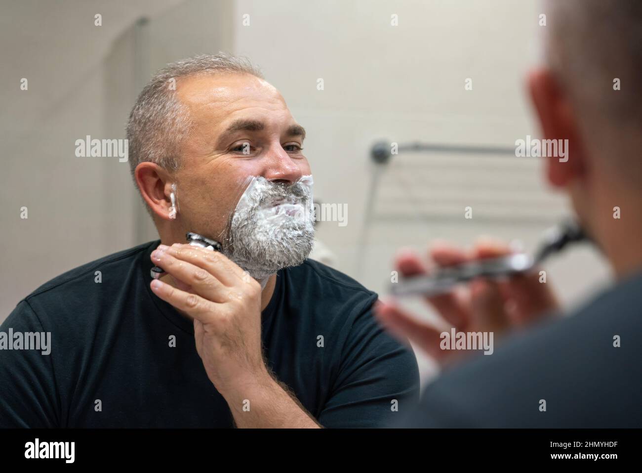 Ein hübscher weißhaariger bärtiger Mann, der sich seinen Bart abrasieren  und in einen Spiegel schaut. Konzept eines sich ändernden Stils  Stockfotografie - Alamy