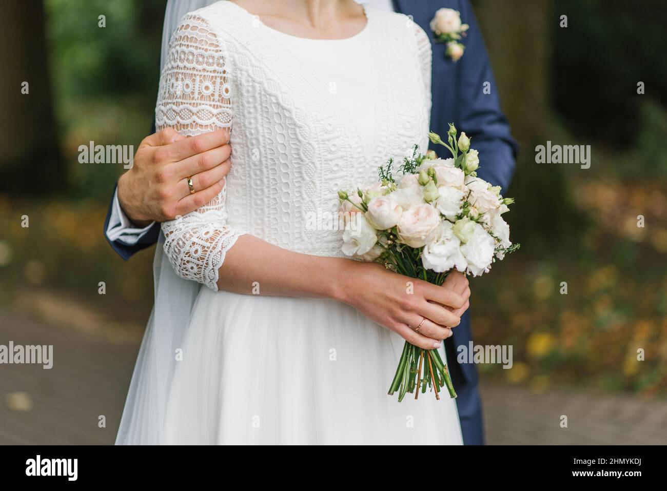 Ein zartes Brautstrauß in den Händen der Braut, die vom Bräutigam umarmt wird Stockfoto