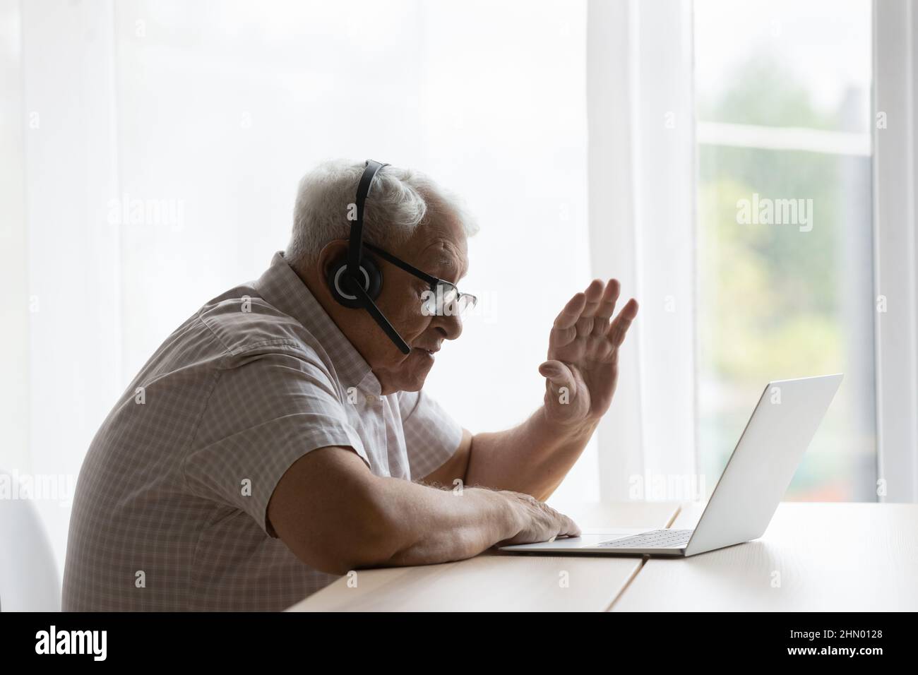Älterer älterer 80s einsamer Mann mit Kopfhörern, der die Hand winkt Stockfoto