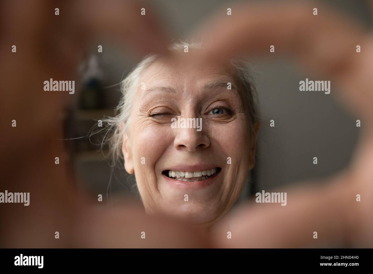 Glückliche ältere Dame winkend auf Kamera durch Hand Finger Herz Stockfoto