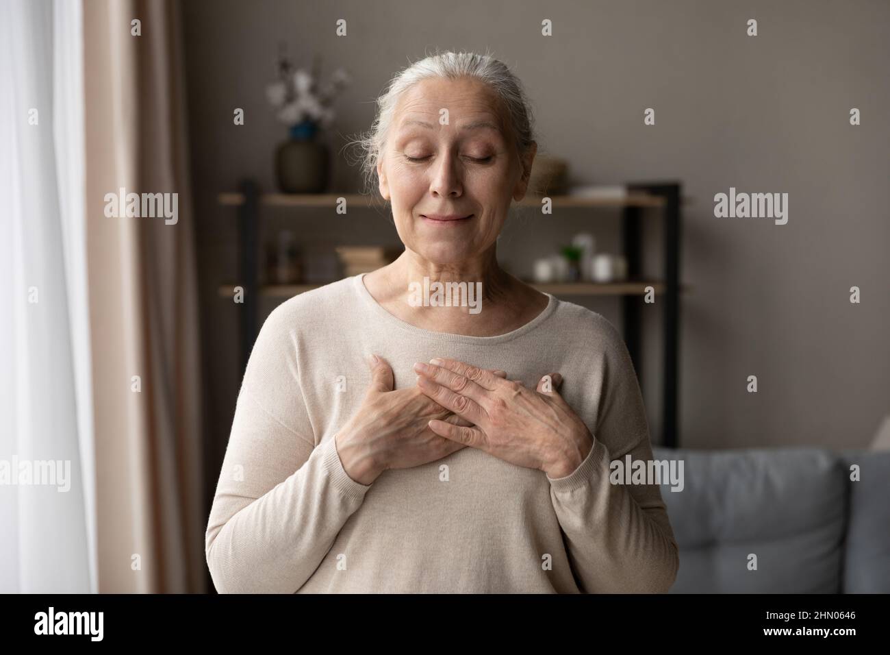 Glücklich dankbar ältere Dame posiert zu Hause mit geschlossenen Augen Stockfoto