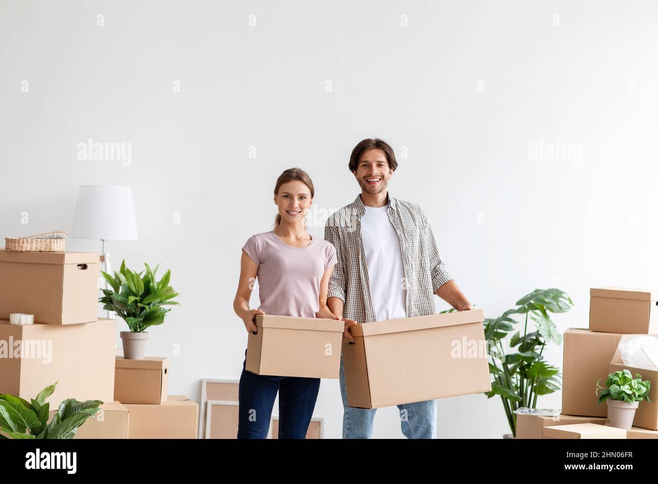 Zufriedene europäische Millennials-Dame und -Mann in legeren Kartons mit Habseligkeiten im Zimmer, leerem Raum Stockfoto