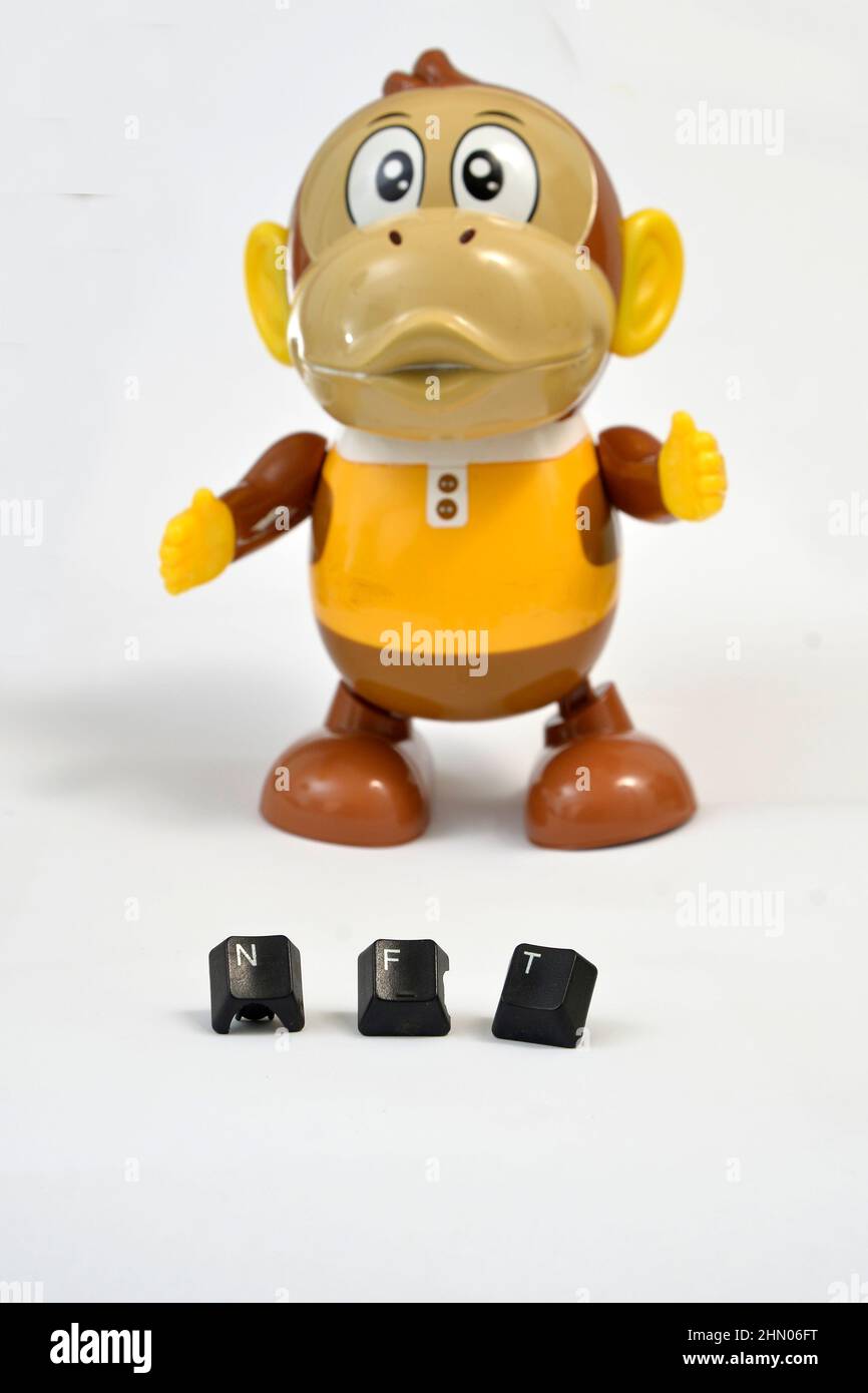 NFT-Text mit gebrauchten schwarzen Computerschlüsseln vor Plastik-Affenspielzeug auf weißem Hintergrund. Stockfoto