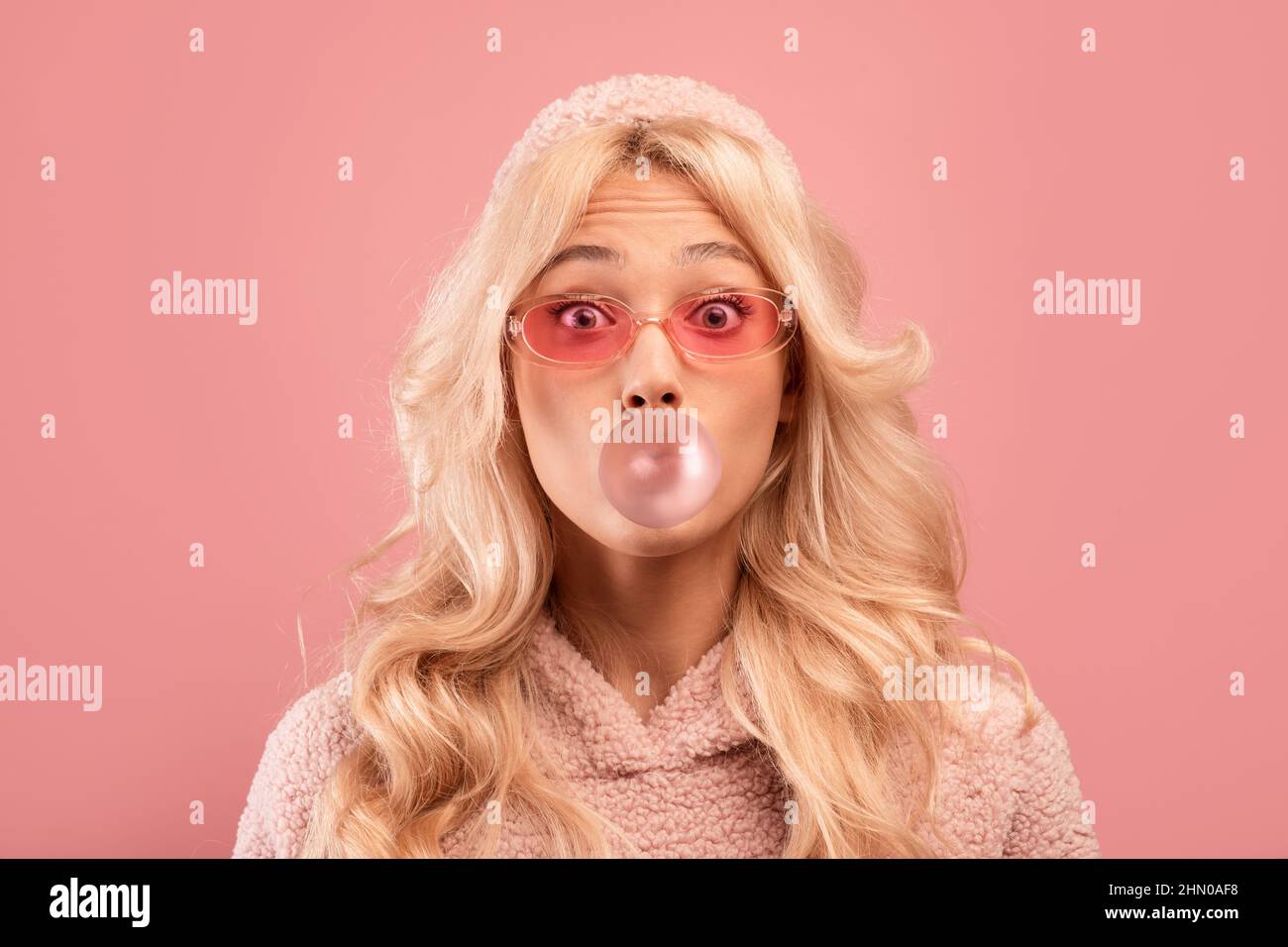 Fröhliche blonde Dame Kaugummi kauen und Blase blasen, Blick auf die Kamera auf rosa Studio-Hintergrund Stockfoto
