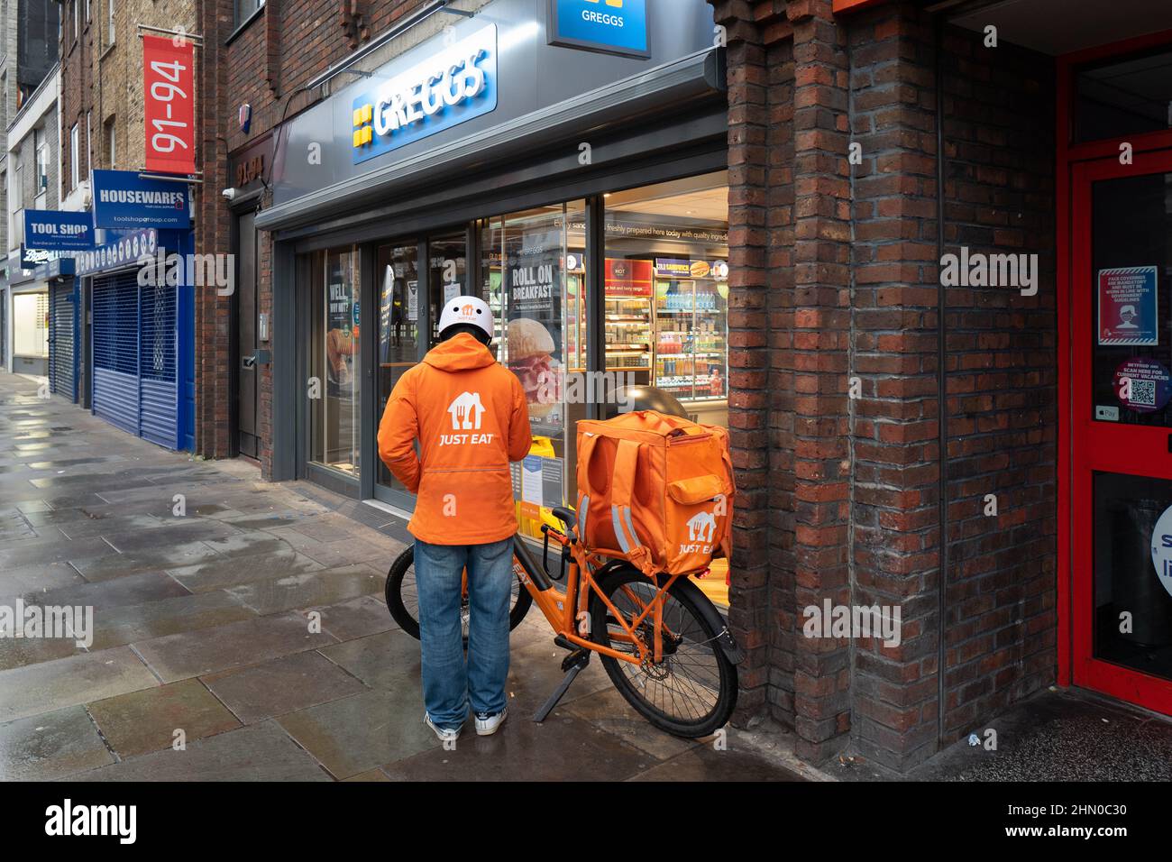 Ein Just Eat Delivery Person macht sich bereit, Greggs eingeben, um eine Bestellung für die Lieferung zu sammeln. Am frühen Sonntagmorgen in Lower Marsh, Waterloo London, aufgenommen Stockfoto