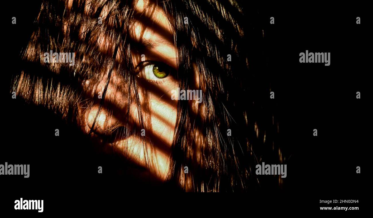 Ein Mädchen mit grünen Augen blickt verängstigt von der Kamera weg. Die Schatten der Fensterläden sind ihr gegenüber zu sehen. Stockfoto