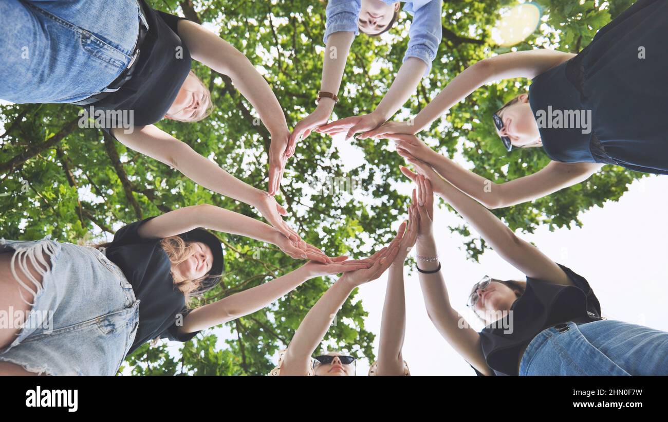 Die Freundinnen verbinden ihre Handflächen in einem Kreis vor dem Hintergrund von Ästen. Stockfoto