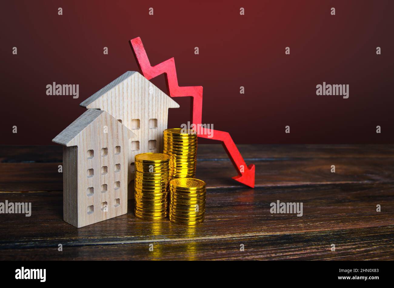 Roter Pfeil nach unten und Häuser. Fallender Immobilienmarkt. Niedrige Wohnungspreise. Reduzierte Hypothekenzinsen. Krise. Wartungskosten. Rezession. Gehäuseblasen Stockfoto