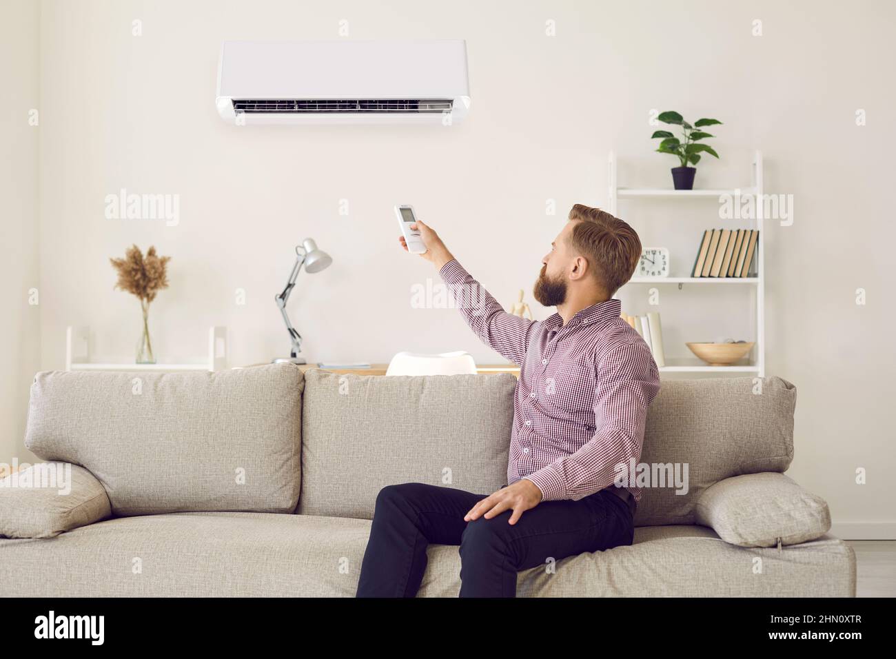 Der Mieter schaltet die Klimaanlage im Wohnzimmer ein Stockfoto