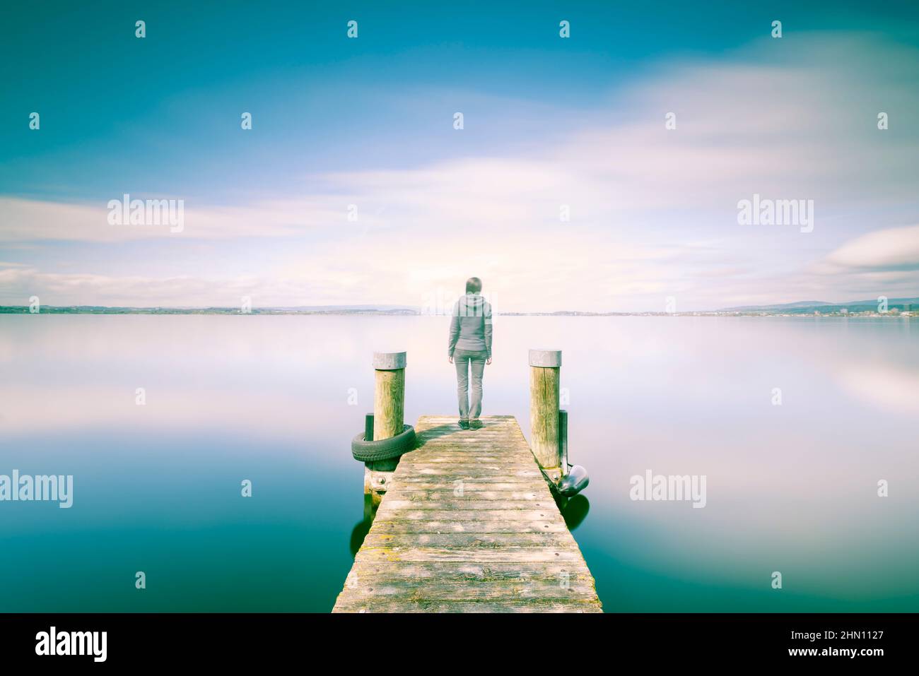 Doppelte Belichtung. Weibliche Figur auf einem hölzernen Steg. Das Ufer des Sees, eine lange Exposition. Minimalismus, Selbstreflex, Meditation. Stockfoto