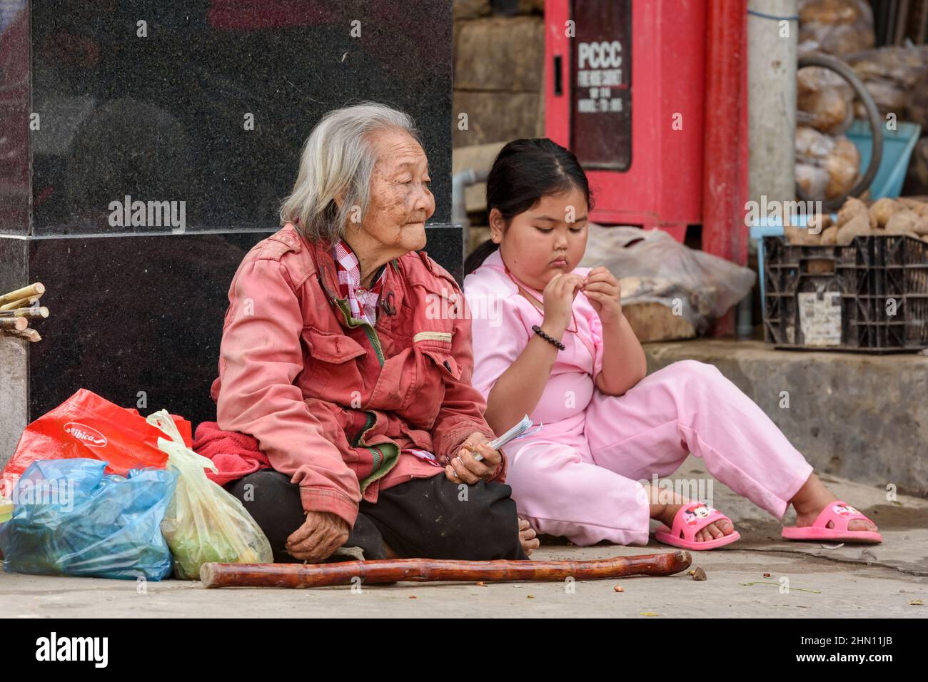 Ein junges Mädchen und eine Großmutter sitzen auf dem geschäftigen Lebensmittelmarkt in Cai Rang, in der Nähe von Can Tho, Mekong Delta, Südvietnam, unter Lebensmittelhändlern Stockfoto