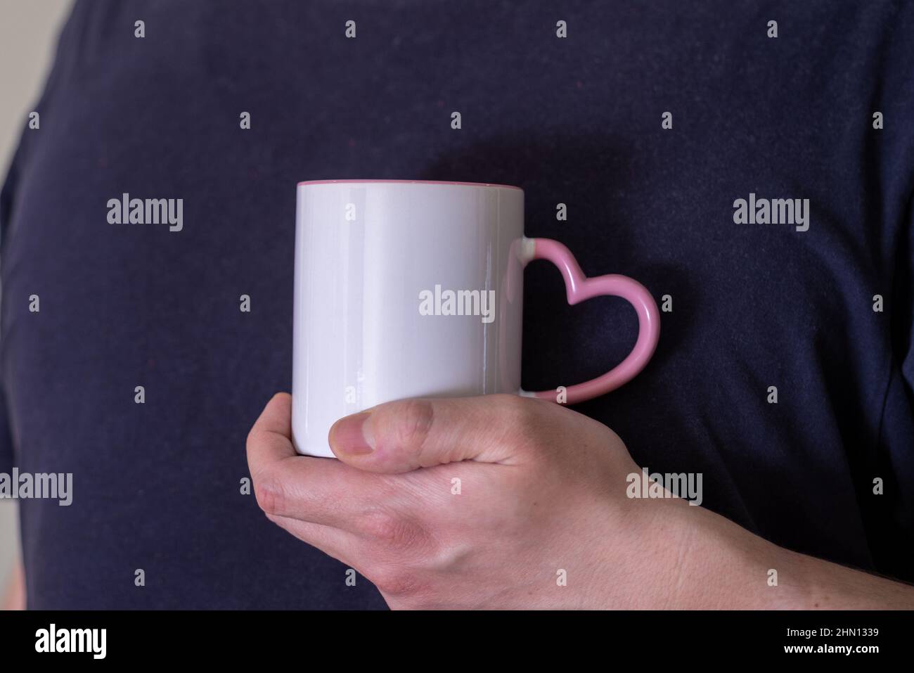 Mann, der eine weiße Tasse heißes Getränk im Freien hält. Die Hand eines Mannes hält einen leeren Becher vor schwarzem Hintergrund. Nahaufnahme, Mockup-Bild, Kopierbereich für Text Stockfoto