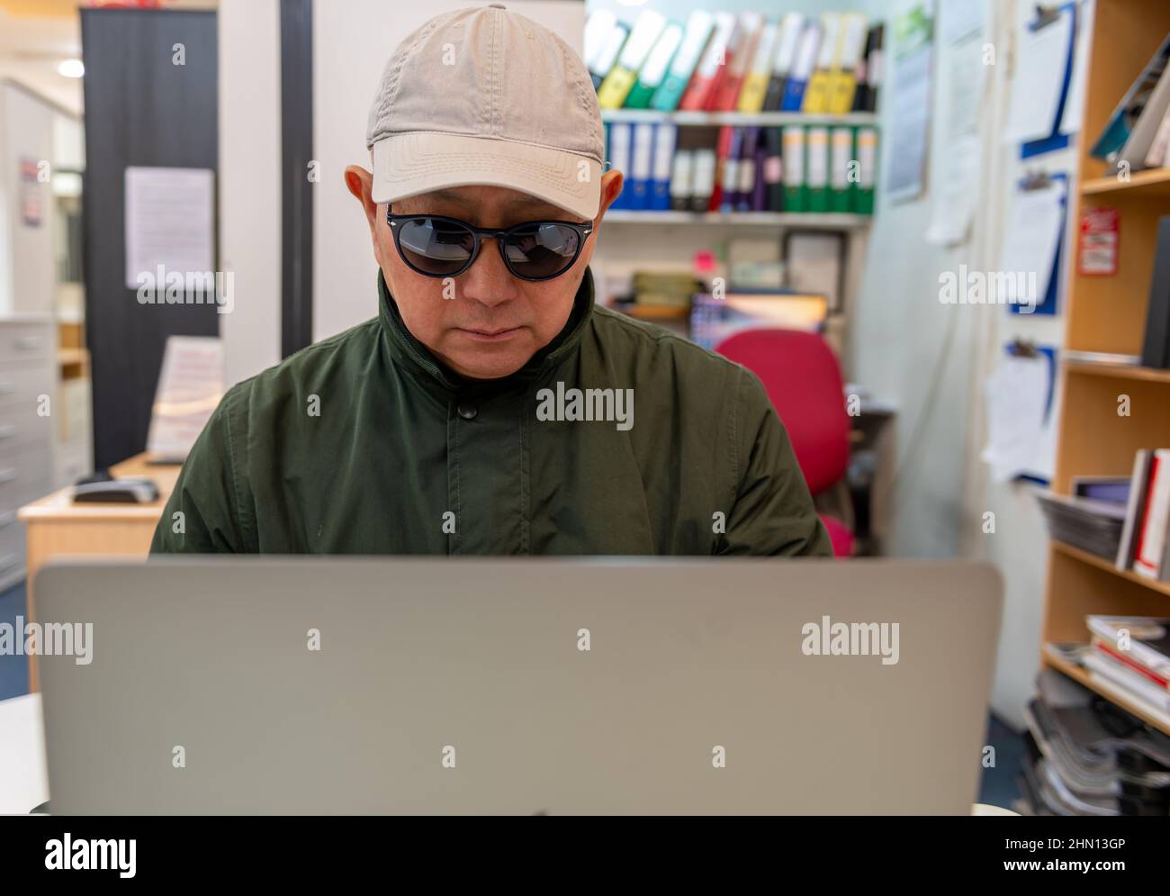 Ein Mann, der online einen Laptop mit Sonnenbrille und Mütze trägt. Konzept für Cyberkriminalität, Sicherheit, Finanzbetrug. Stockfoto