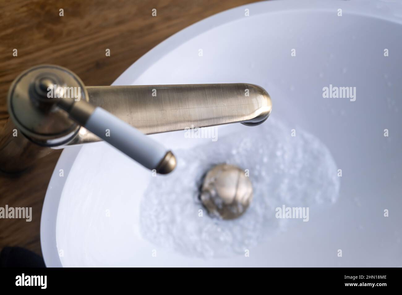 Waschbecken Wasserhahn, Badezimmer Inneneinrichtung Detail. Öffnen Sie den bronzenen Wasserhahn mit fließendem Wasser auf dem weißen Waschbecken, Nahaufnahme von oben Stockfoto