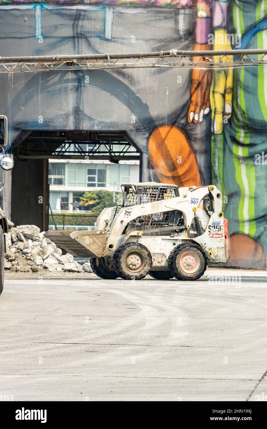 Minibagger-Planierraupe vor bemalten Wandmalereien auf Zementsilos auf Granville Island Vancouver British Columbia kanada Stockfoto