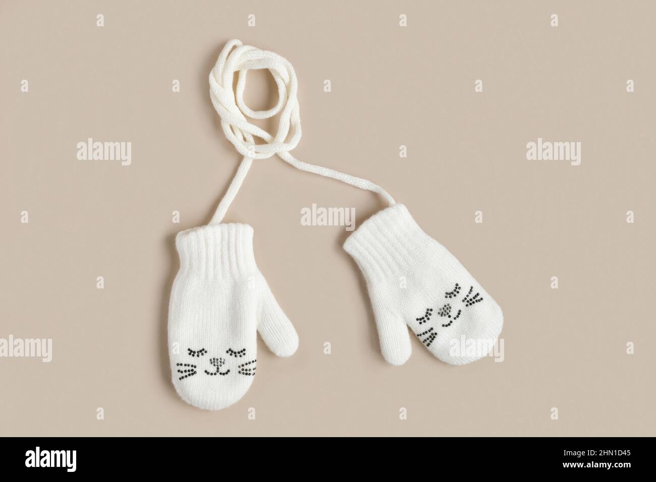 Weiß gestrickte Babyhandschuhe isoliert auf einem natürlichen beigen Hintergrund, Draufsicht. Winterkleidung für Kinder. Fäustlinge mit Lächeln. Kleine Babyhandschuhe Stockfoto