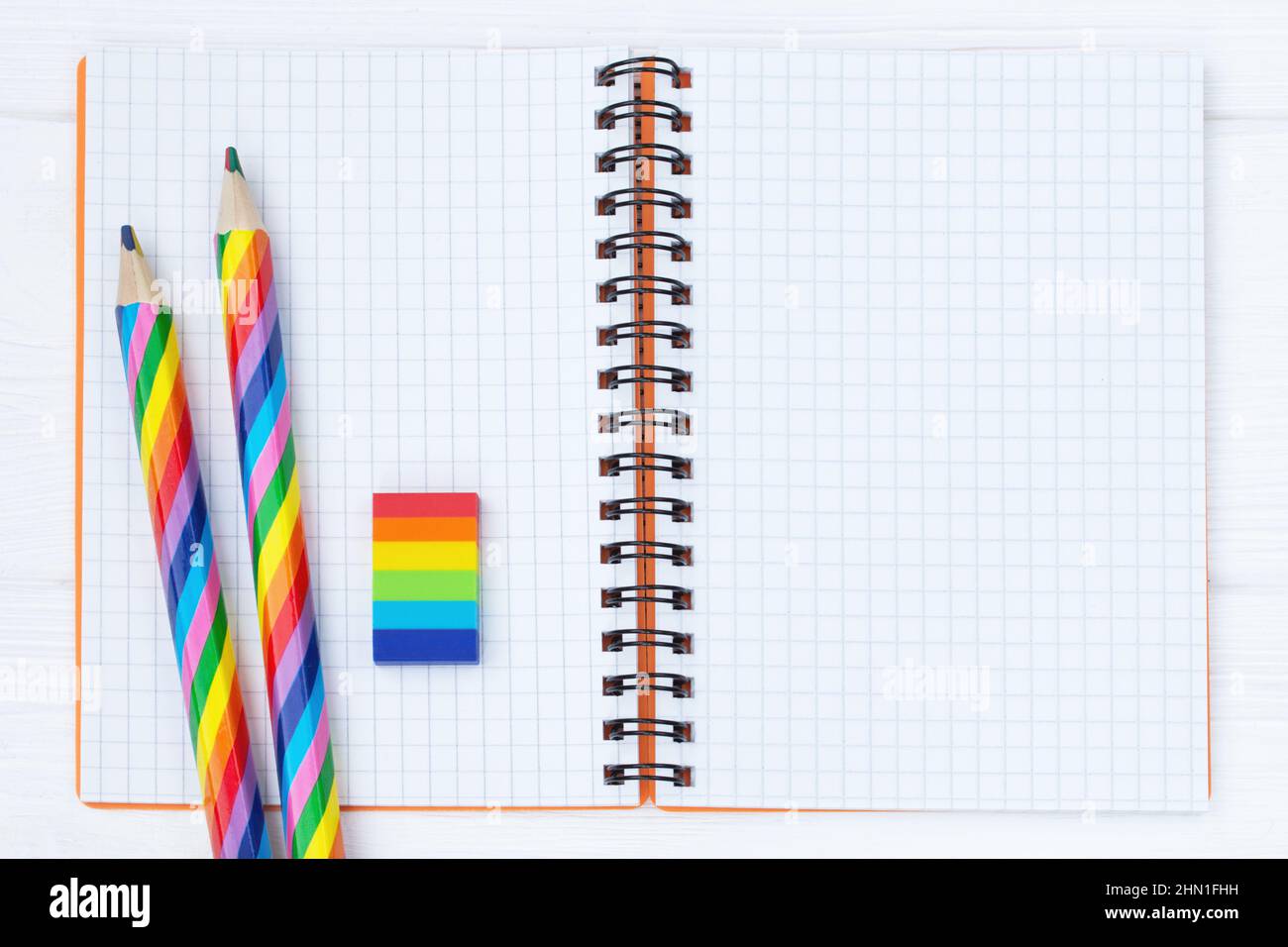 Offenes Copybook mit zwei regenbogenfarbenen Bleistiften und einem Gummi auf weißem Holztisch Stockfoto