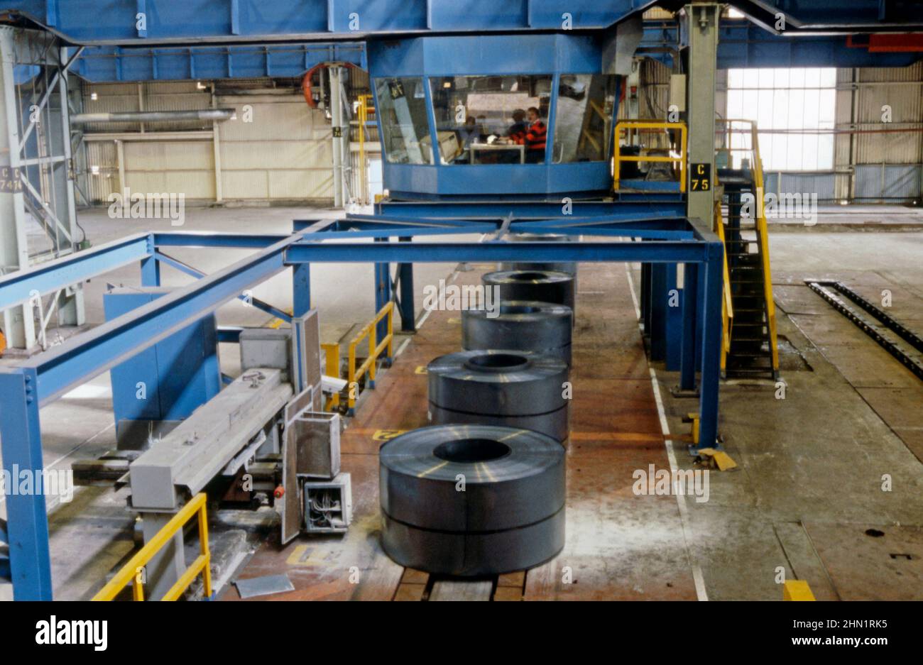 Ein Blick Mitte 1980s in das Stahlwerk von Port Talbot, einem integrierten Stahlproduktionswerk in Port Talbot, West Glamorgan, Wales, Großbritannien. Im Inneren des Werks werden fertig gebundene Blechrollen in die Produktionslinie unterhalb des Schaltwarte verschoben. Dieses Bild stammt aus einer Vintage-Farbtransparenz, die von einem Gastfotografen aufgenommen wurde – einem Vintage-Foto aus dem Jahr 1980s. Stockfoto