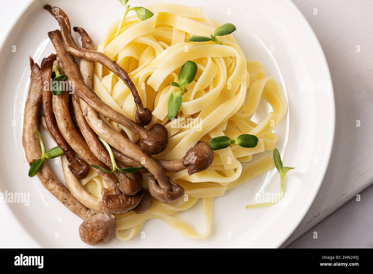 Nahaufnahme von gekochten Shimeji und Nudeln, Teller mit gebratenen Pilzen und Pasta, auf weißem Teller. Stockfoto