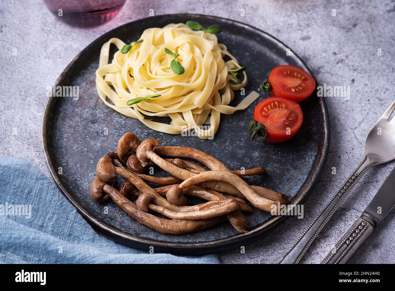 Pasta mit gebratenen Pilzen, gekochten Shimeji und Nudeln auf dem Teller auf grauem Hintergrund. Stockfoto