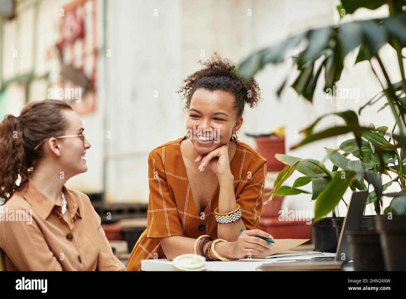 Junge lächelnde Biracial Gärtnerin und ihre kaukasische Kollegin, die Diskussion über die Inneneinrichtung ihres neuen Floristen-Shops Stockfoto