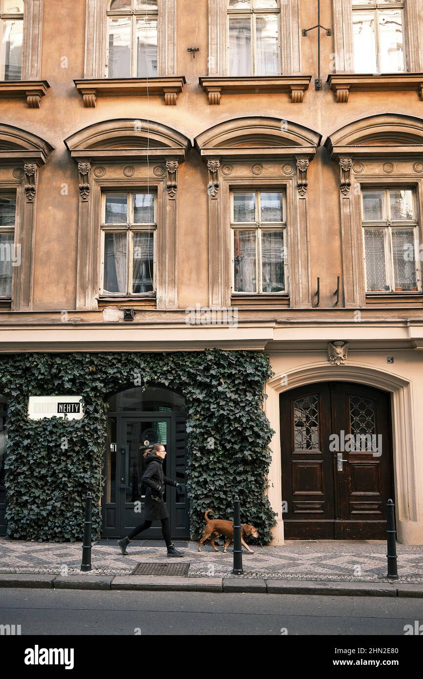 Eine Dame, die mit einem Hund vor einem neoklassizistischen Gebäude im Zentrum von Prag läuft Stockfoto