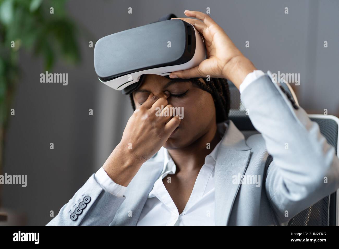 Junge afroamerikanische Geschäftsfrau, die unter Augenbelastung leidet, nachdem sie am Arbeitsplatz ein VR-Headset verwendet hat Stockfoto