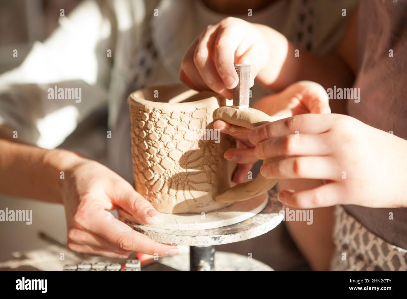 Nicht erkennbares Kind, das Keramik mit Briefmarken schmückt und der Mutter beim Töpferunterricht hilft Stockfoto