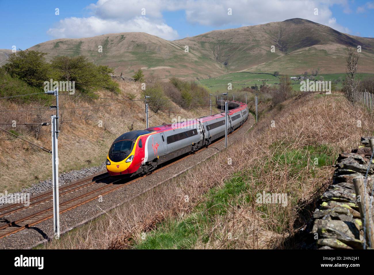 Virgin Trains Alstom Pendolino Kippzug 390132 in der Landschaft Cumbrias auf der elektrifizierten Hauptlinie der Westküste, kippend um eine Ecke Stockfoto