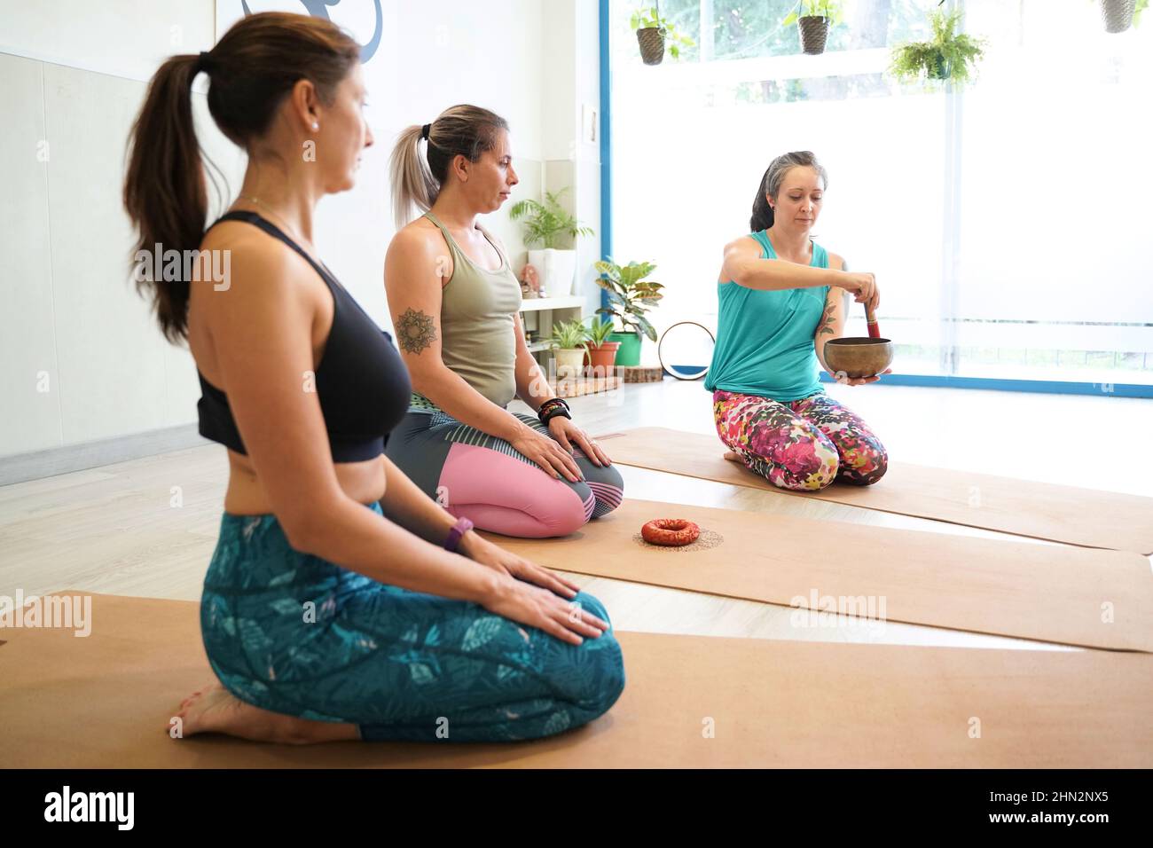 Menschen praktizieren Yoga und Meditation im Studiokurs, Lehrer spielen tibetische Schale und singen Mantra Stockfoto